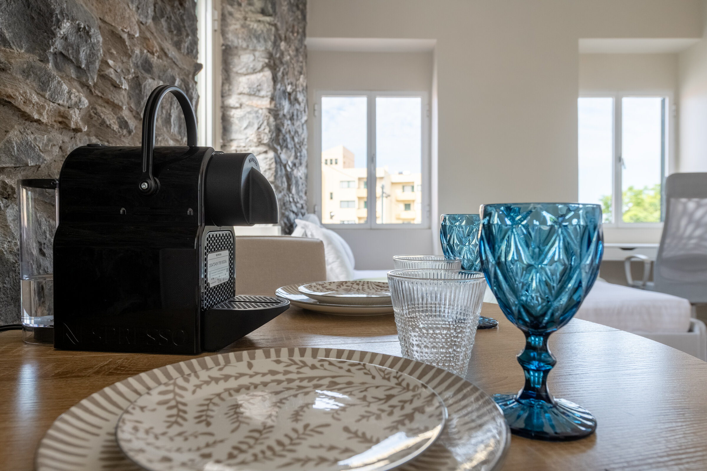 Dining table set with glassware, kitchenette with coffee machine in the background