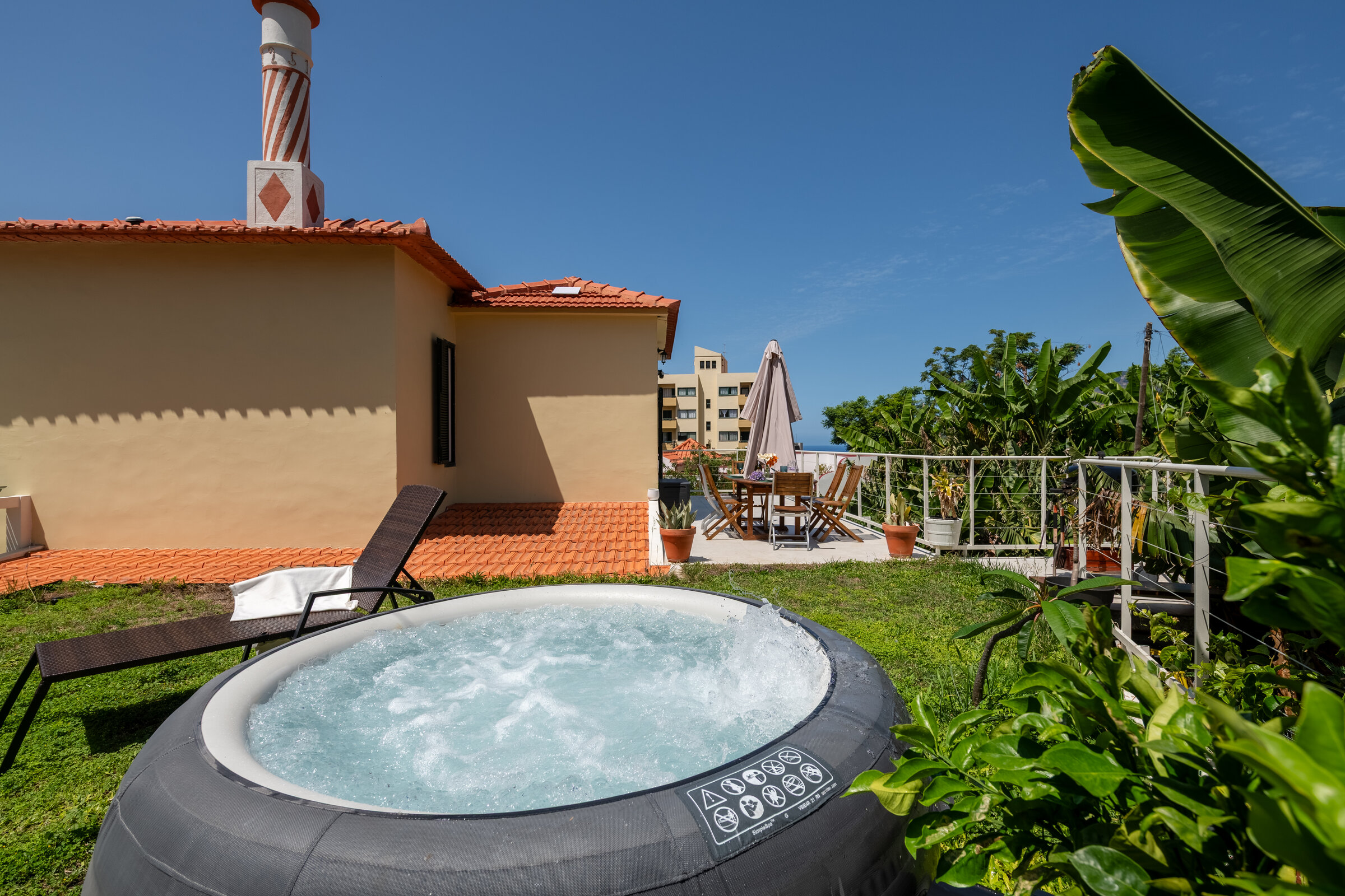 Shared garden jacuzzi bubbling beside the villa, sun loungers and dining table beyond
