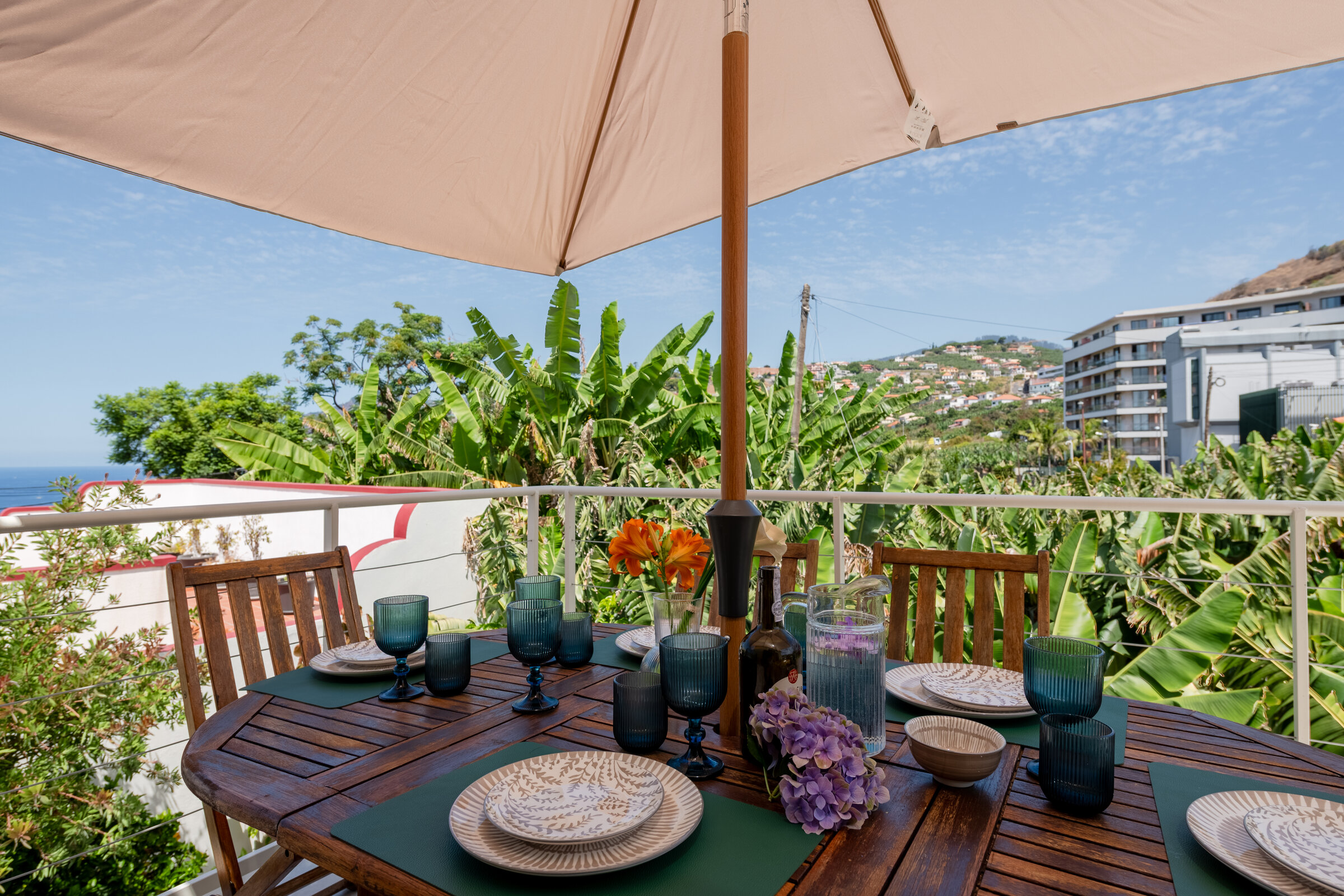 Outdoor dining table set on the balcony beneath an umbrella, ocean view